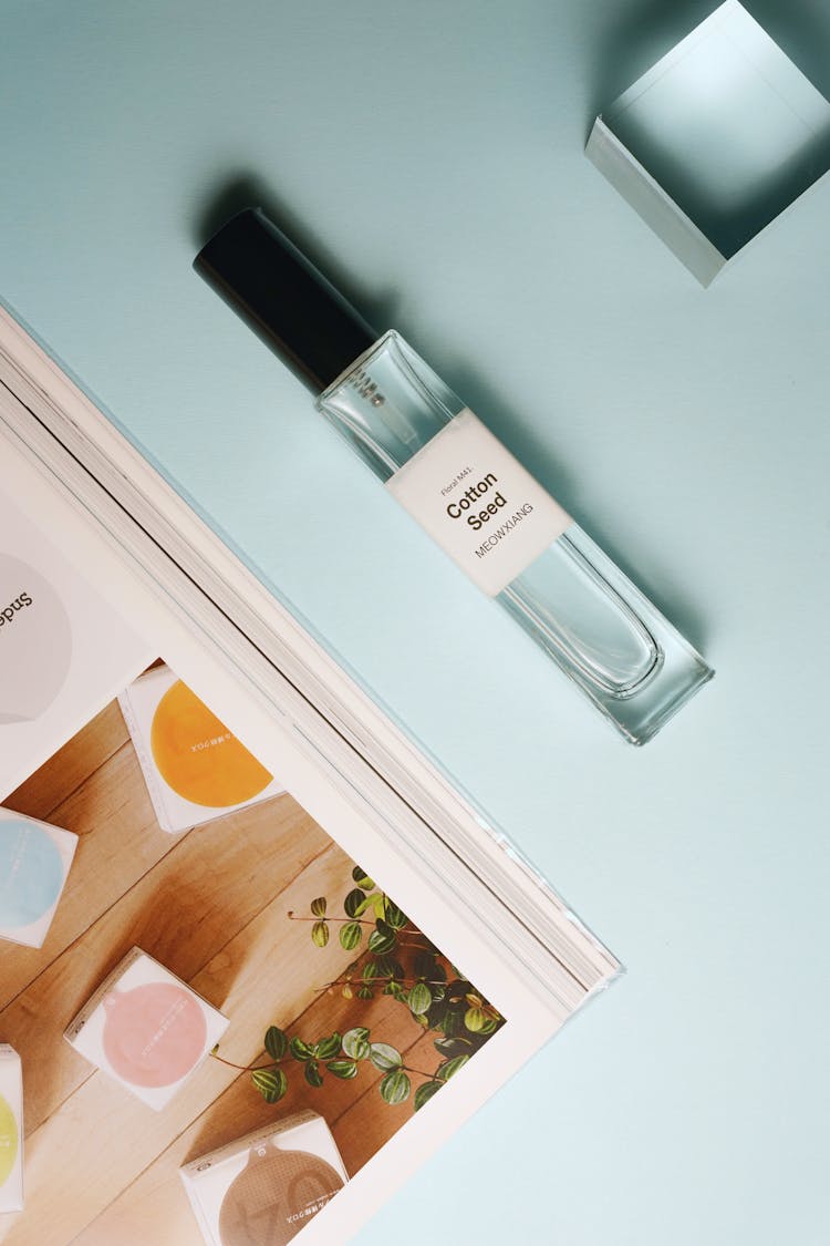 Small Perfume Flask Lying On White Surface Next To Catalogue