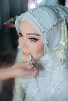 A beautiful bride in traditional attire having makeup applied, showcasing elegance and detail.