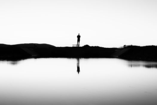 Silhouette of a person standing by a lake with reflections, evoking mystery and solitude.