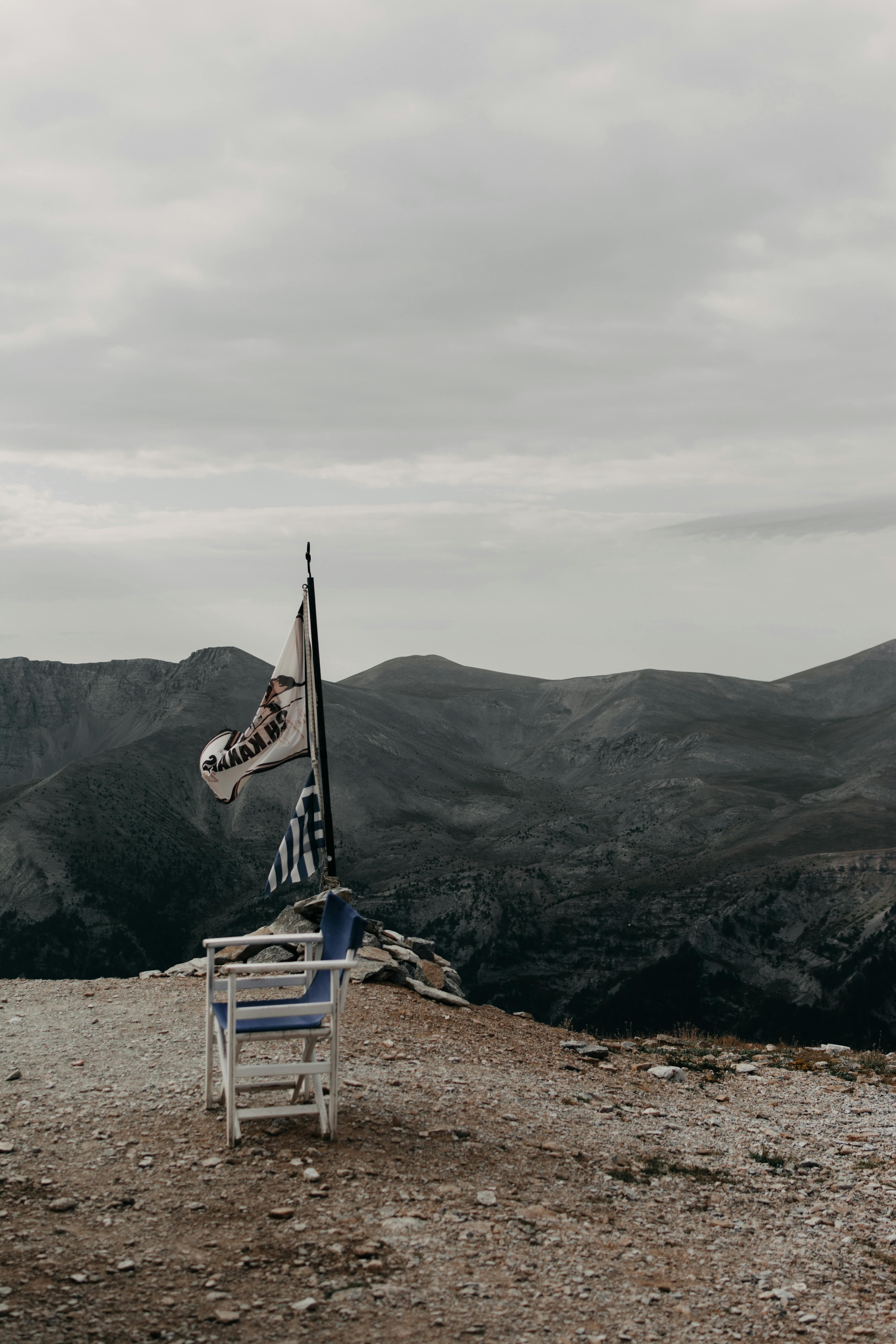 A scenic mountain landscape with a Greek flag near a solitary chair, evoking serenity.