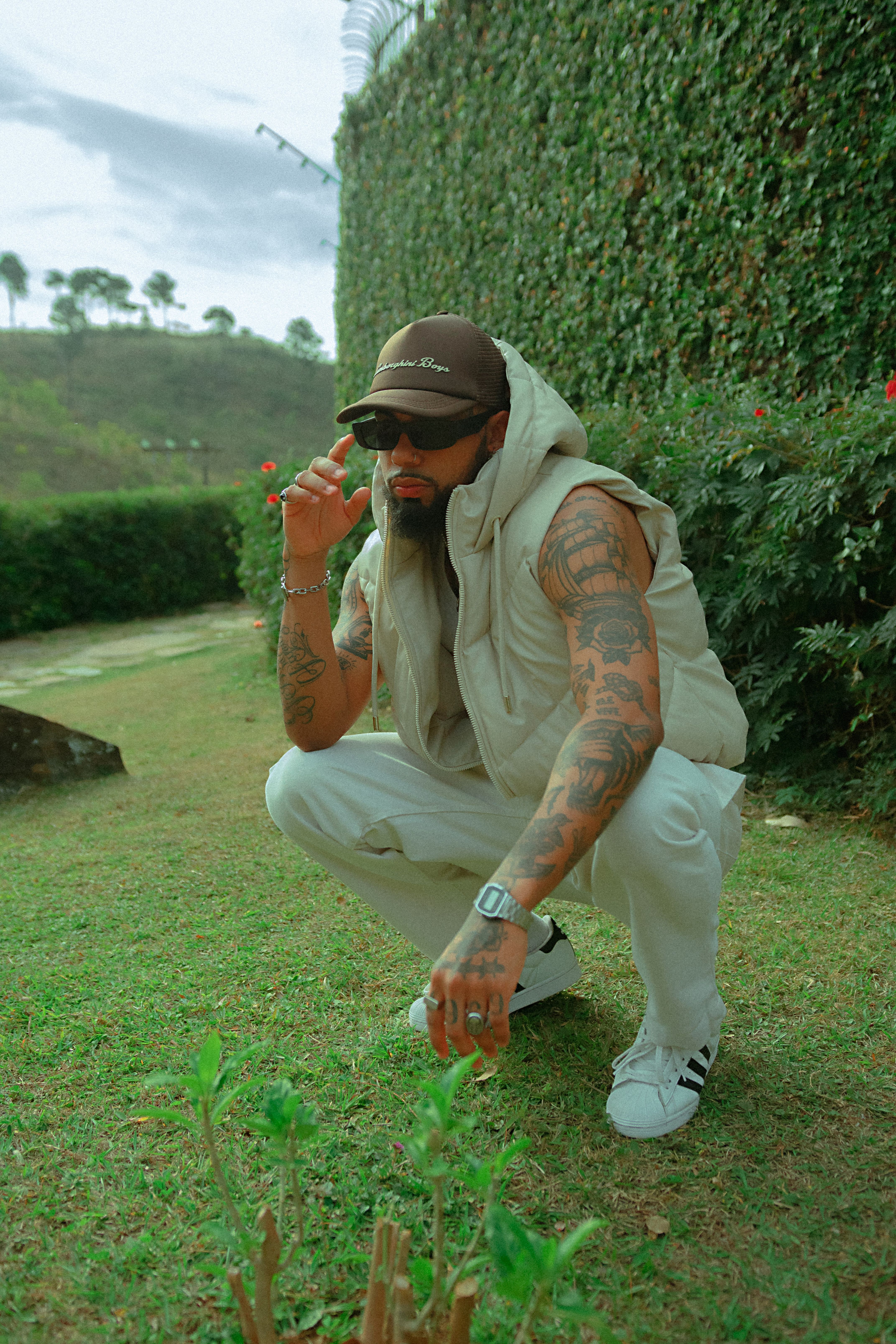 Modern portrait of a tattooed man squatting outdoors in Belo Horizonte, Brazil, showcasing style and fashion.