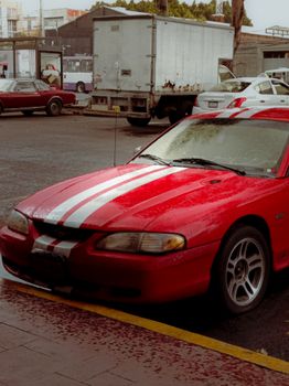 Stylish red car with white stripes parked in an urban street, highlighting automotive design.