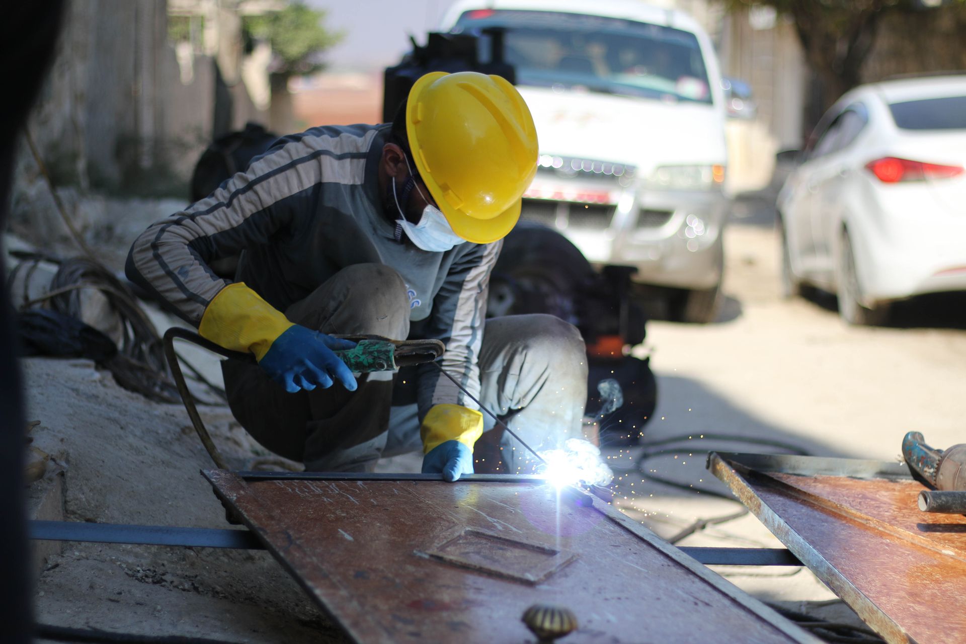 Skilled worker welding metal outdoors wearing safety gear with bright sparks.