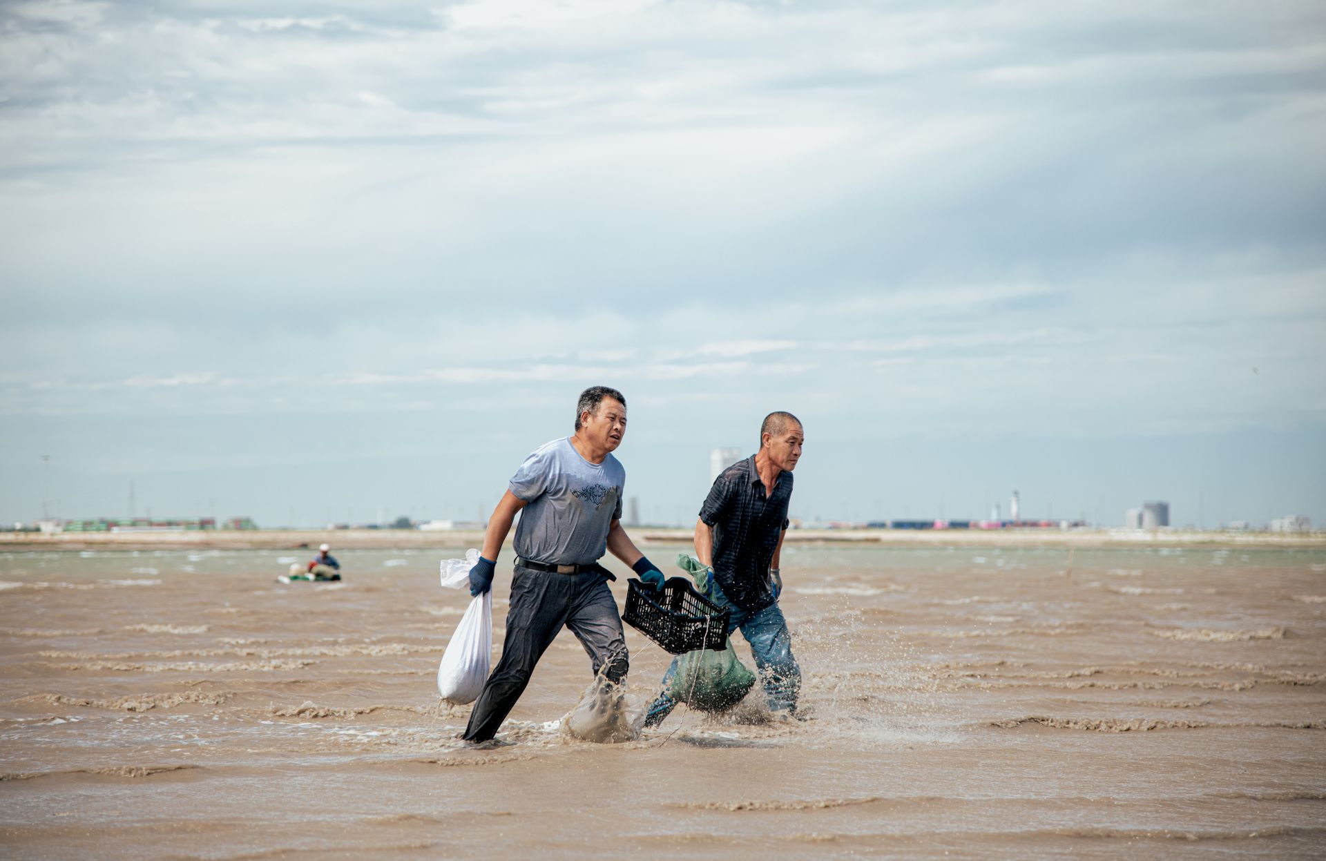 Men Walking on Brown Body of Water While Carrying Sacks