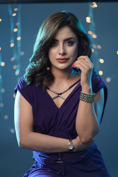 Free Elegant woman in a purple dress posing confidently indoors with a string lights backdrop. Stock Photo