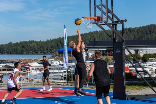 Energetic basketball game on a lakeside court with young men jumping and playing.