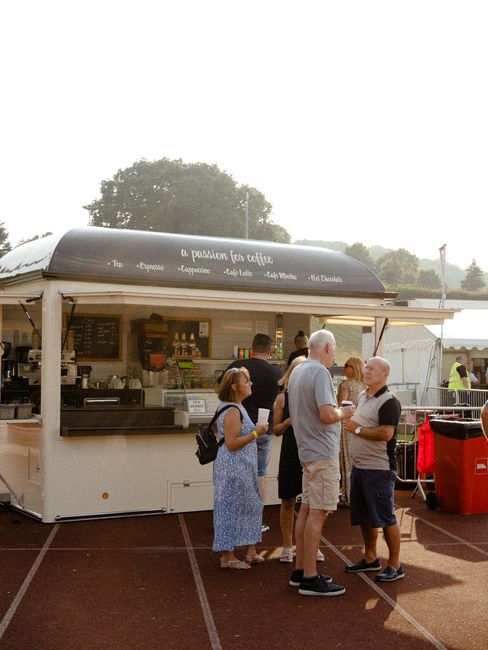 Group of adults enjoy drinks at an outdoor coffee stand on a sunny day.