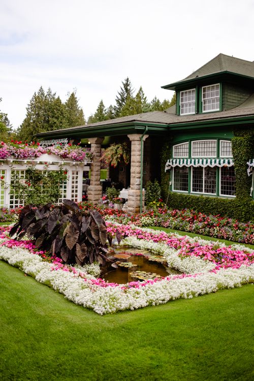 Free A beautifully landscaped garden with vibrant flowers in front of a classic green house, showcasing timeless elegance. Stock Photo