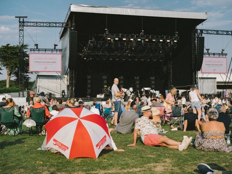 A vibrant outdoor music festival with a crowd enjoying the event, seated and relaxed.