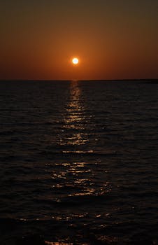 A stunning sunset over the ocean, casting golden reflections on the calm water surface.