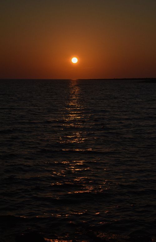 Free A stunning sunset over the ocean, casting golden reflections on the calm water surface. Stock Photo