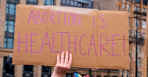 Free Cardboard sign reading 'Abortion is Healthcare!' held at a public protest event. Stock Photo