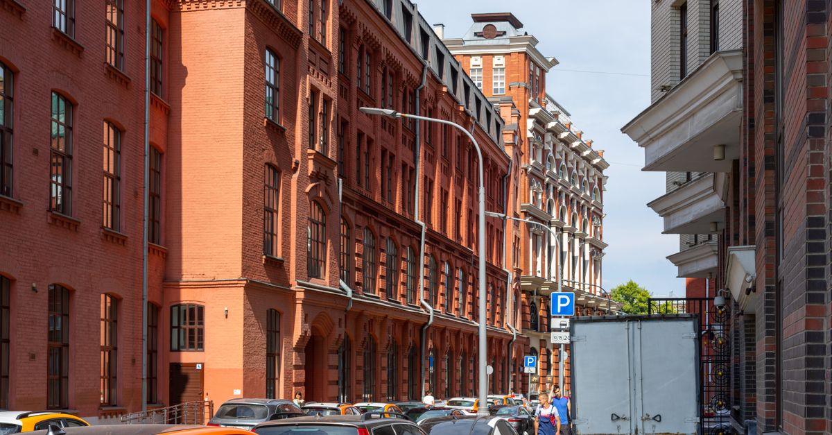 City street with historic red brick buildings and parked cars on a sunny day.