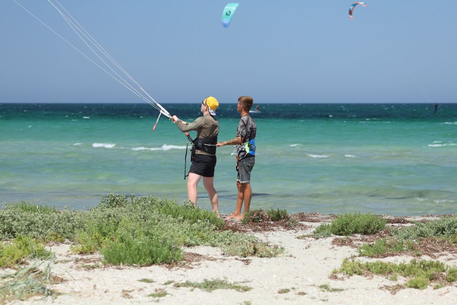 Two young men practicing kitesurfing on a sunny beach, enhancing skills with guidance.