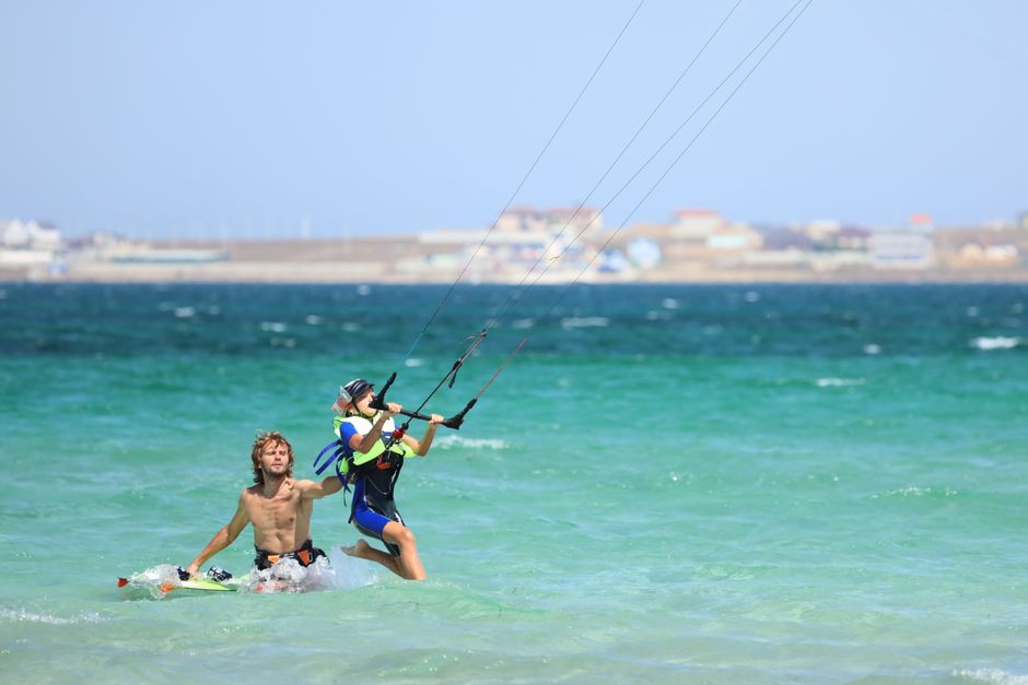 A young kitesurfer guided by an instructor on a sunny beach, perfect for summer activities.