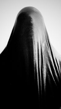 A black and white image of a mysterious figure draped in fabric, creating an enigmatic silhouette.