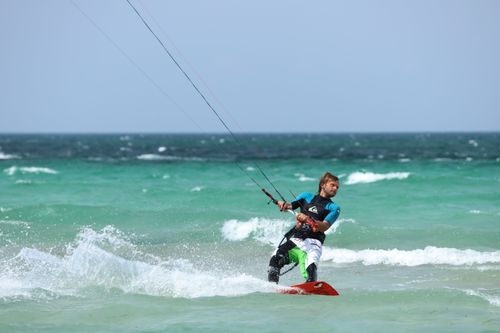Free Experience the thrill of kiteboarding as an athlete rides ocean waves under a clear sky. Stock Photo