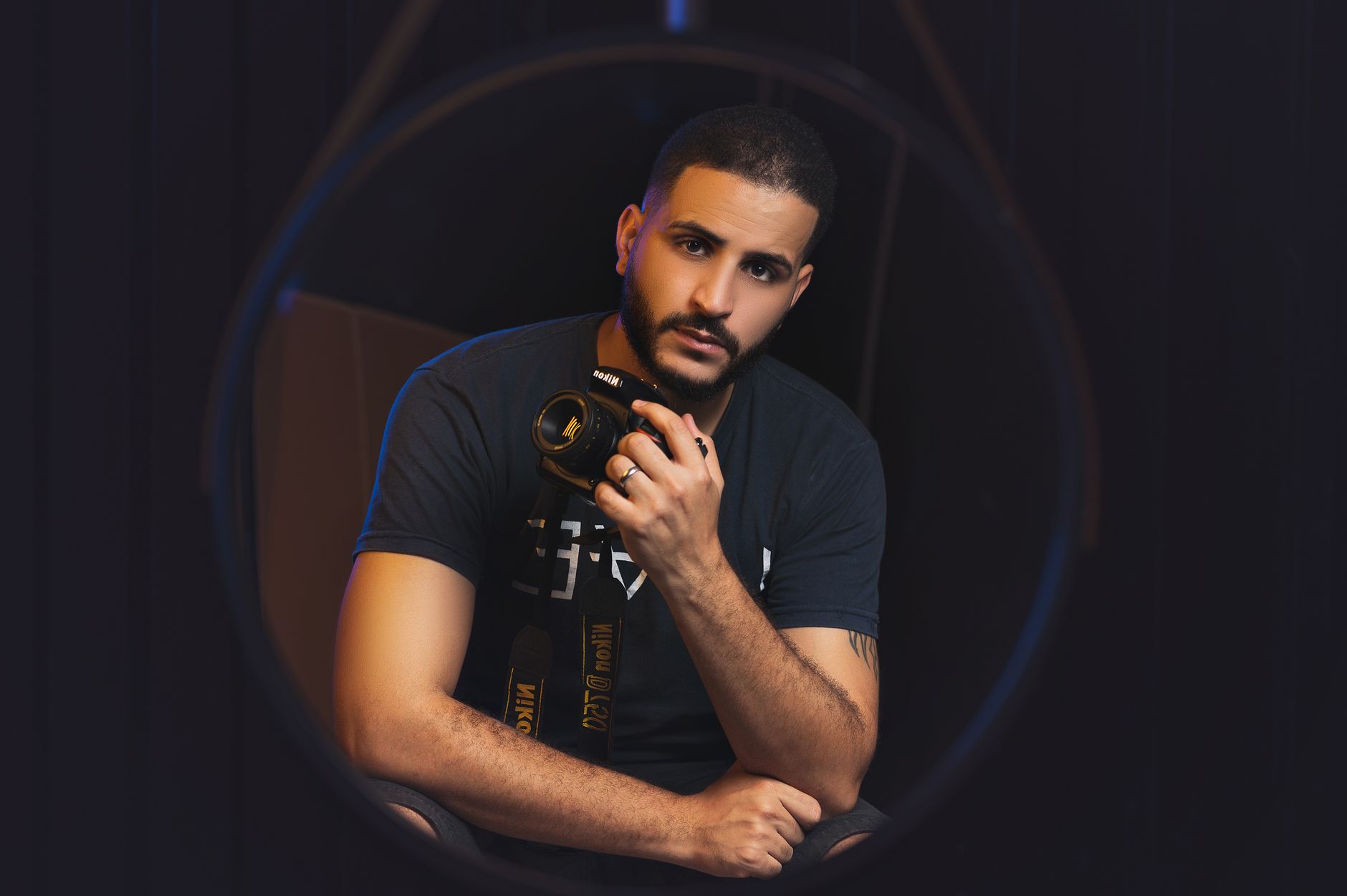 Professional photographer posing with a camera in a dark studio setting.