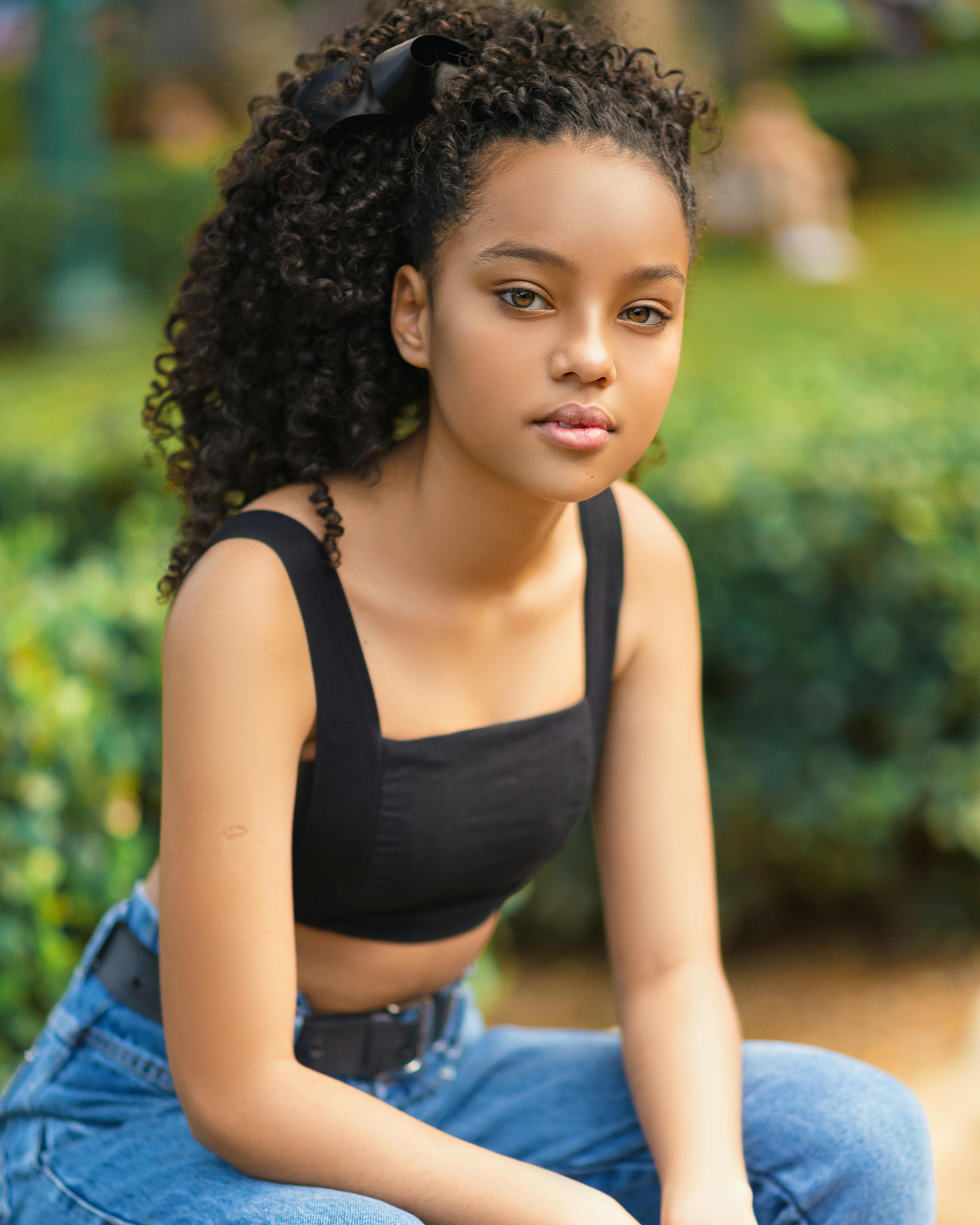 A young girl with curly hair and a black crop top sitting outdoors