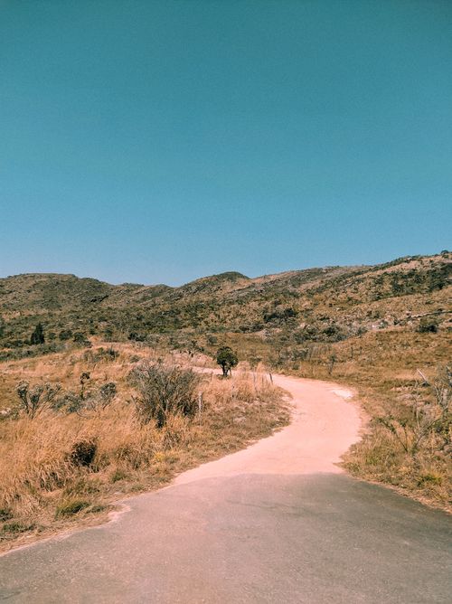 Free Explore the winding dirt road in Santana do Riacho, Brazil, surrounded by hills and grassy terrain under a clear sky. Stock Photo