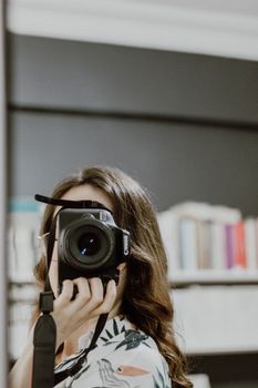 Brunette woman taking a photo indoors, holding a camera with a floral top.