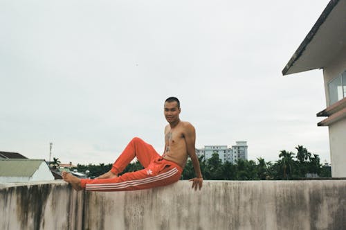 Shirtless Man Sitting on Concrete Fence