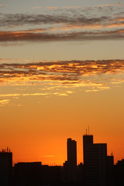 Free Silhouette of city buildings against a vibrant sunset sky with dramatic clouds. Stock Photo