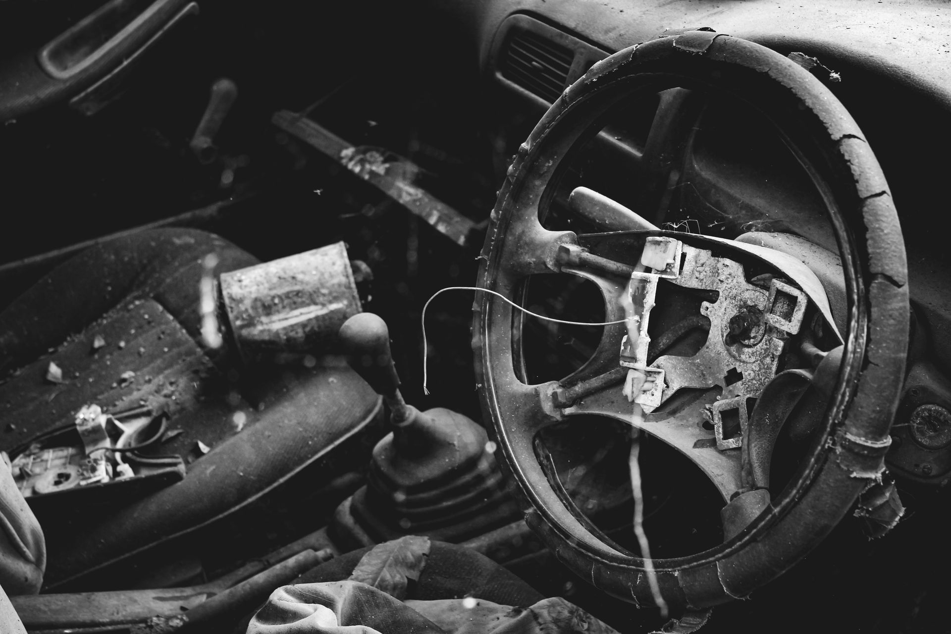 Monochrome image showing a damaged, abandoned car interior with a broken steering wheel.