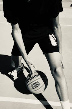 Black and white image of a person playing basketball outdoors, focusing on dynamic movement.