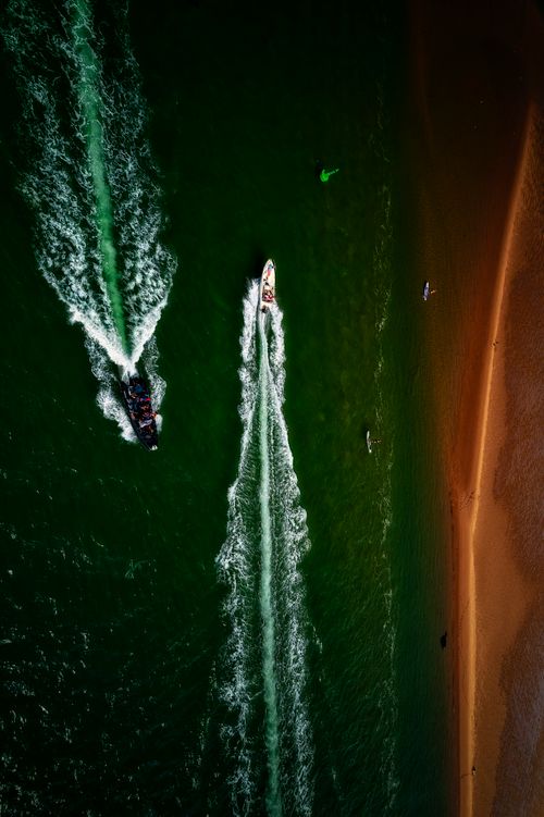 Free Aerial capture of boats and surfers along Exmouth Beach's coastline. Stock Photo