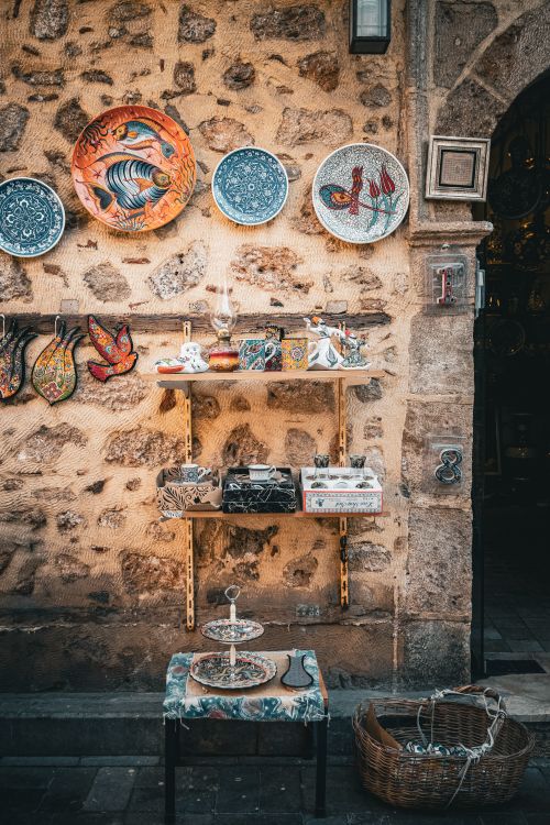 Free Outdoor display of colorful ceramic plates and figurines on a stone wall, creating a rustic aesthetic. Stock Photo
