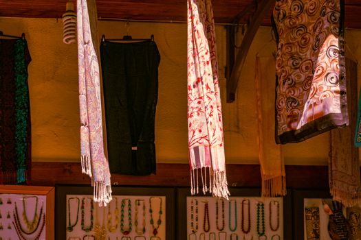 Vibrant fabrics and jewelry adorn a city market stall offering diverse cultural designs.