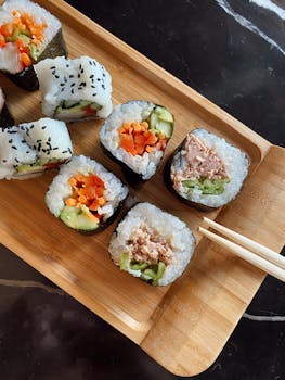 A variety of sushi rolls with vegetables and tuna served on a wooden tray.