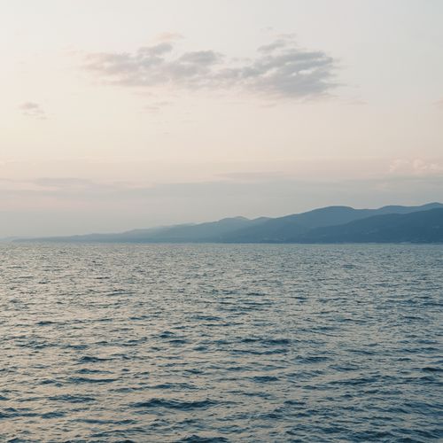 Free Tranquil ocean view with distant mountains and a gentle summer sky, perfect for peaceful landscapes. Stock Photo
