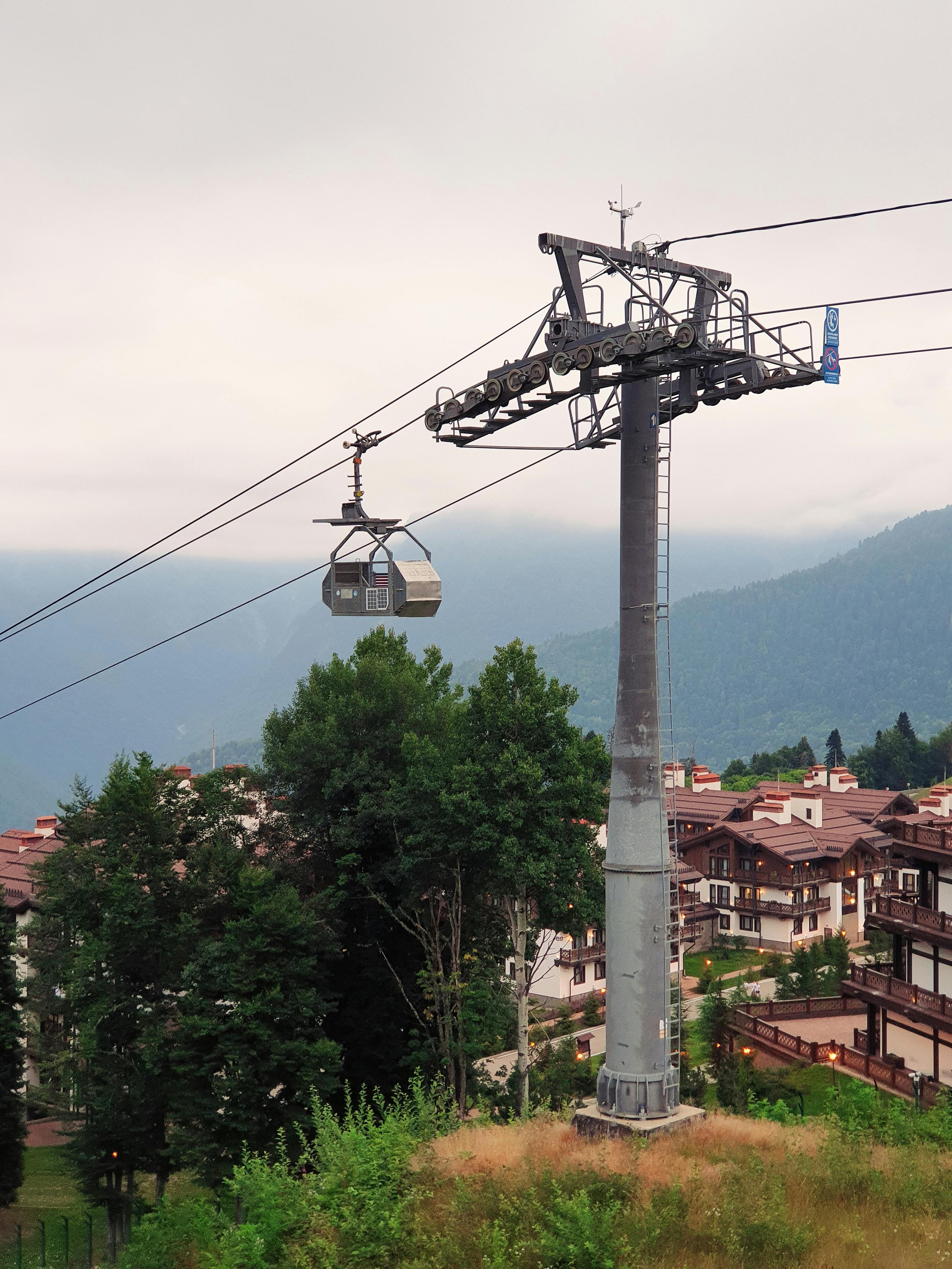 Free Cable car gliding over alpine village with lush greenery and misty mountains. Stock Photo
