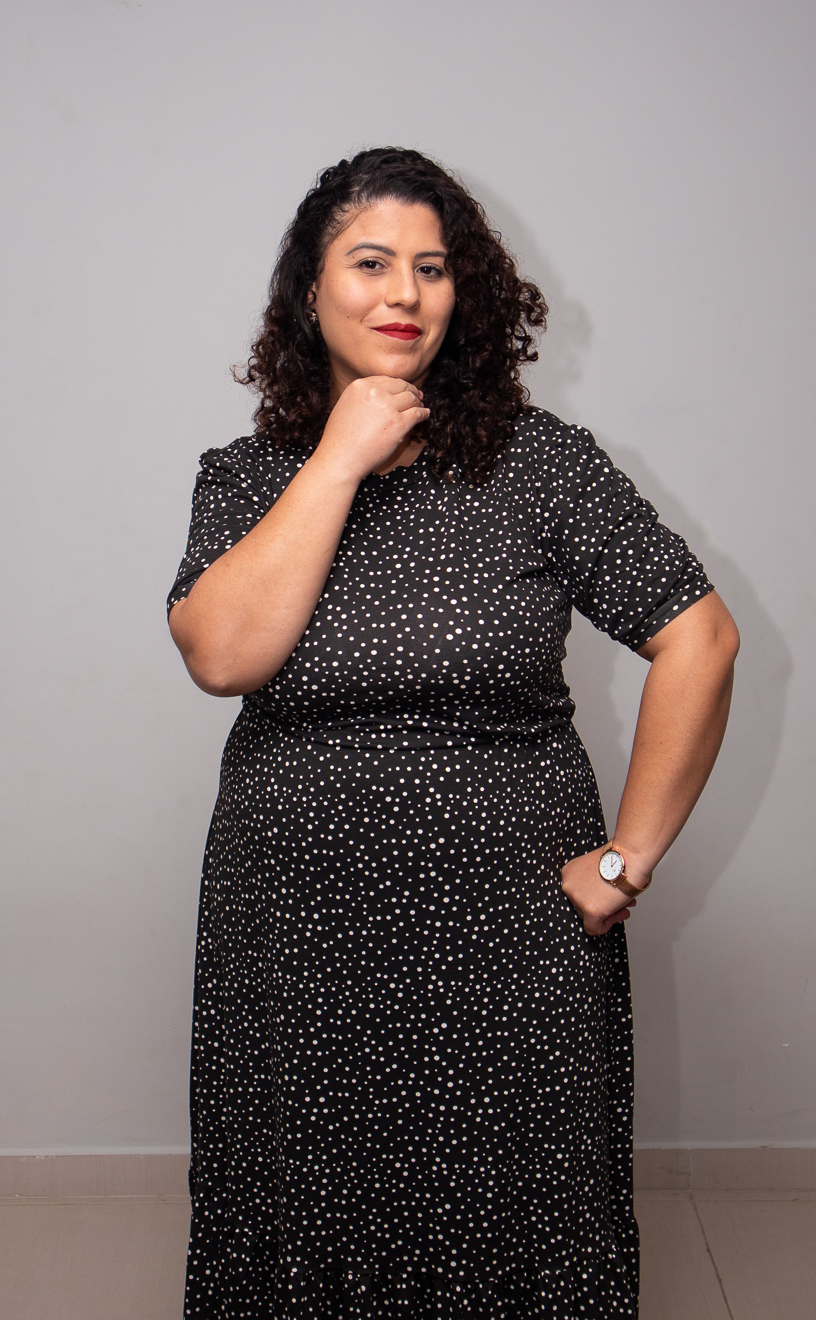 Portrait of a confident woman posing with a charming smile in a polka dot dress against a gray background.
