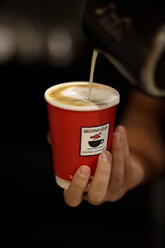 Close-up of a hand pouring milk into a cappuccino at Second Cup in Baku, Azerbaijan.