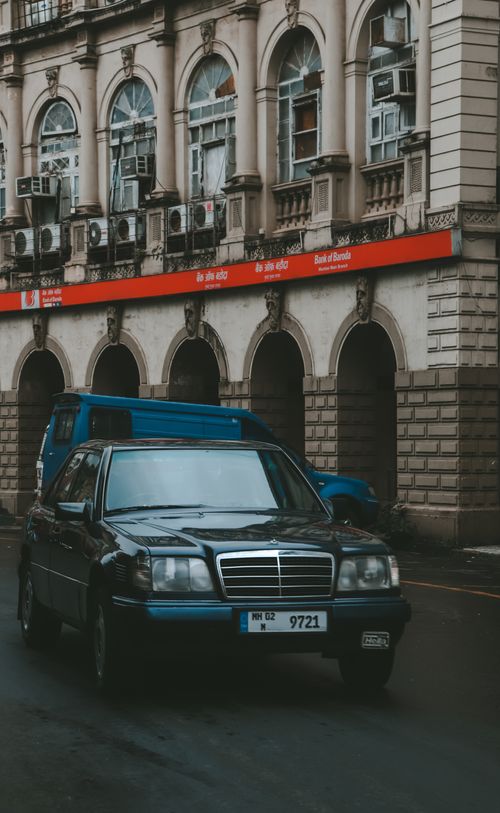 Free A classic black Mercedes driving through an urban street with historical architecture in the background. Stock Photo