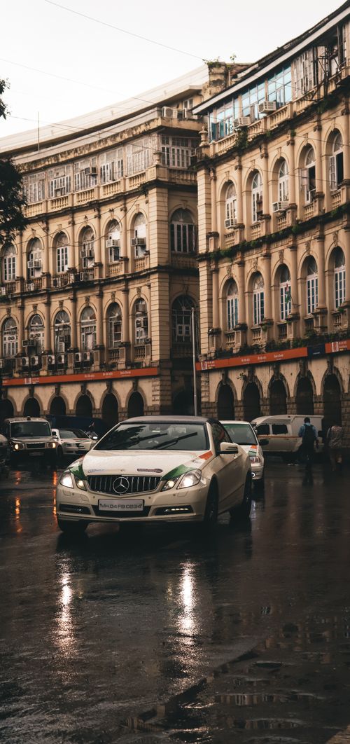 Free A white Mercedes-Benz car navigating through a rainy urban street lined with classic architecture. Stock Photo