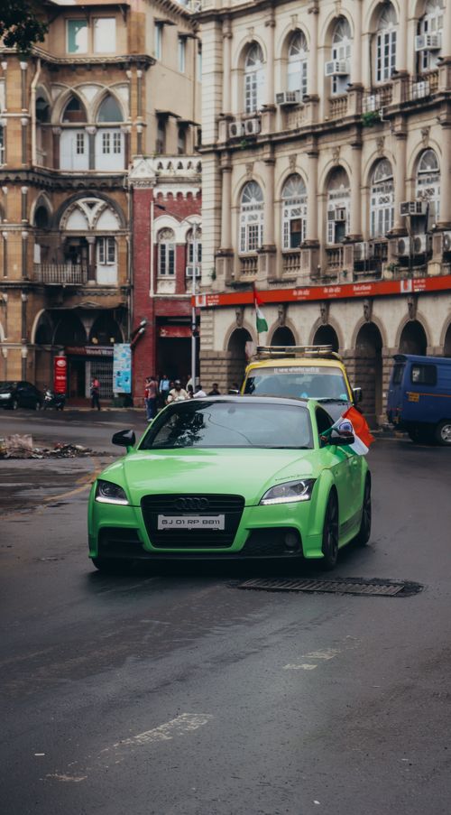 Free Green car on a bustling city street with historic architecture in the background, capturing urban life. Stock Photo