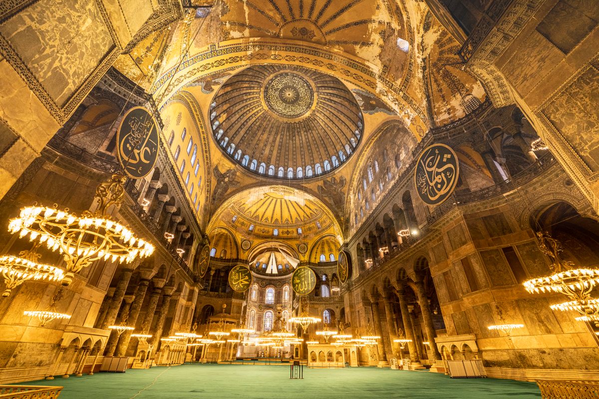Ornate golden mosque interior with a domed ceiling and hanging lamps