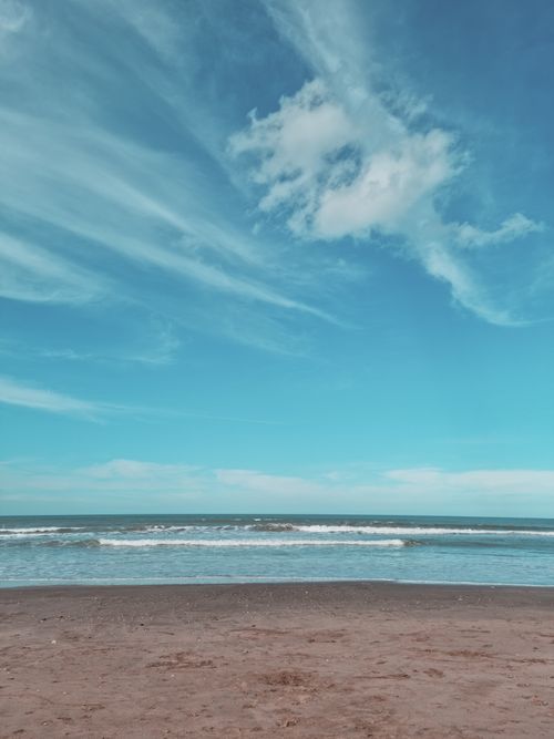 Free Peaceful beach scene with blue skies, rolling waves, and sandy shore for a serene escape. Stock Photo