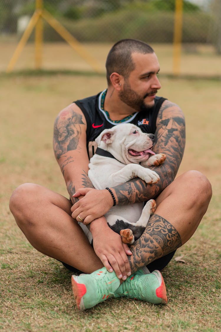 Man Sitting On The Ground Cuddling His Dog