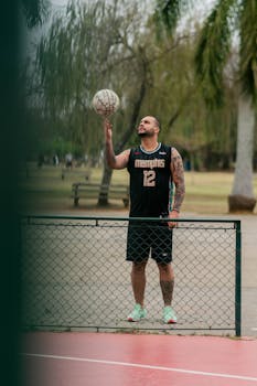 Tattooed man in sportswear balancing a basketball on his finger, showing skill and focus outdoors.