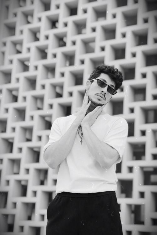 Free Elegant black and white portrait of a young man posing against a grid-patterned wall. Stock Photo