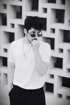 Portrait of a fashionable young man posing with sunglasses in a black and white composition.
