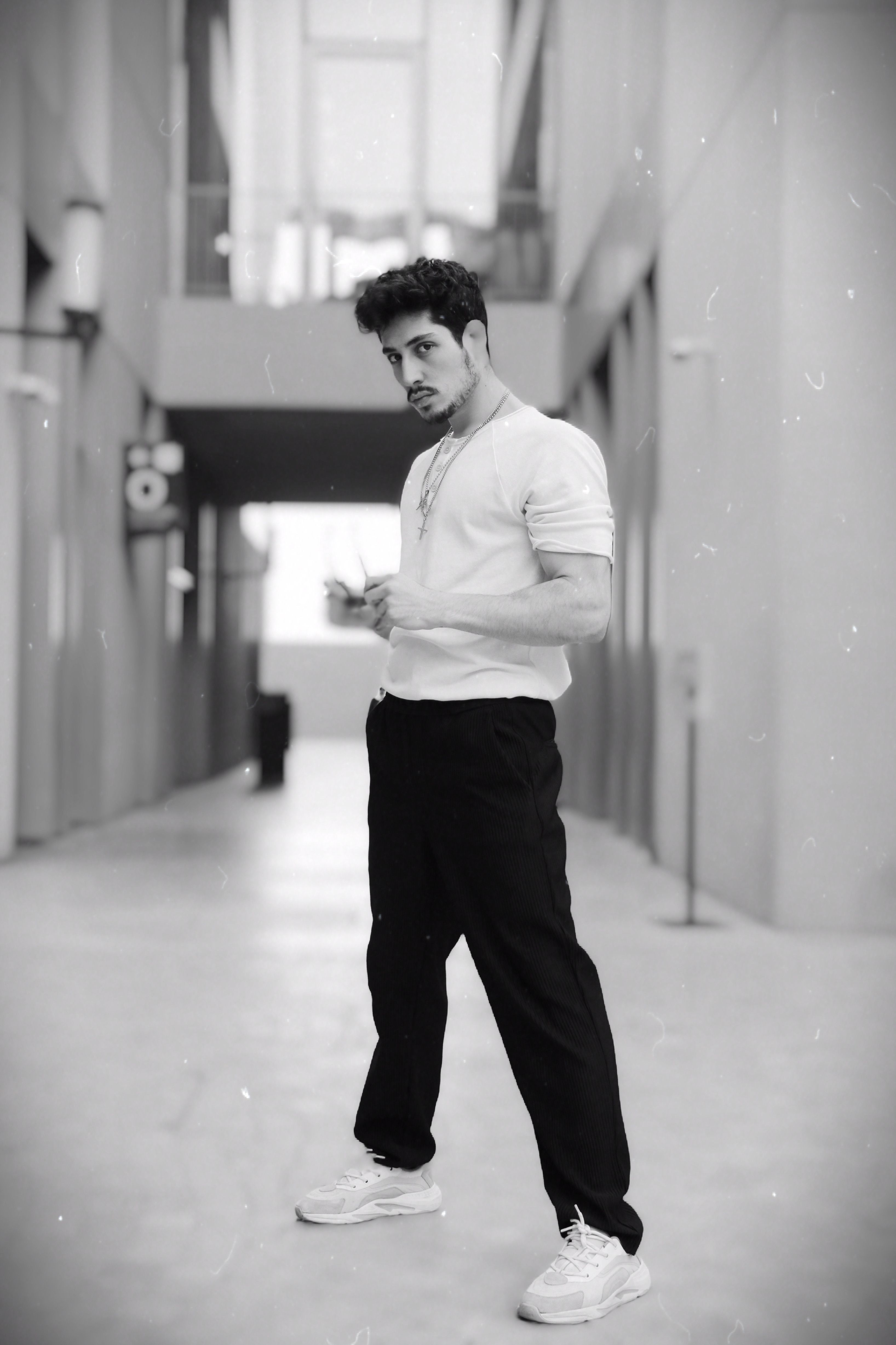 A stylish young man poses confidently in a modern urban alleyway.