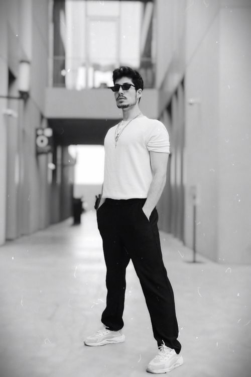 Free Portrait of a young man posing stylishly in an urban alley, exuding confidence and modern fashion. Stock Photo