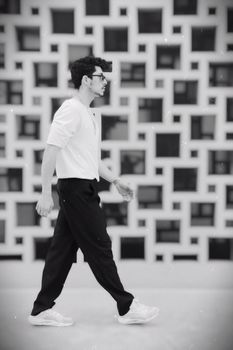 Black and white photo of a man walking stylishly against a geometric patterned wall.