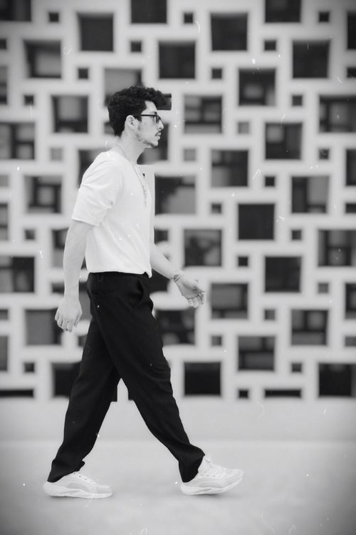 Free Black and white photo of a man walking stylishly against a geometric patterned wall. Stock Photo